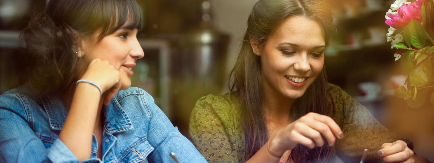 Zwei dunkelhaarige Frauen sitzen im Café und unterhalten sich.