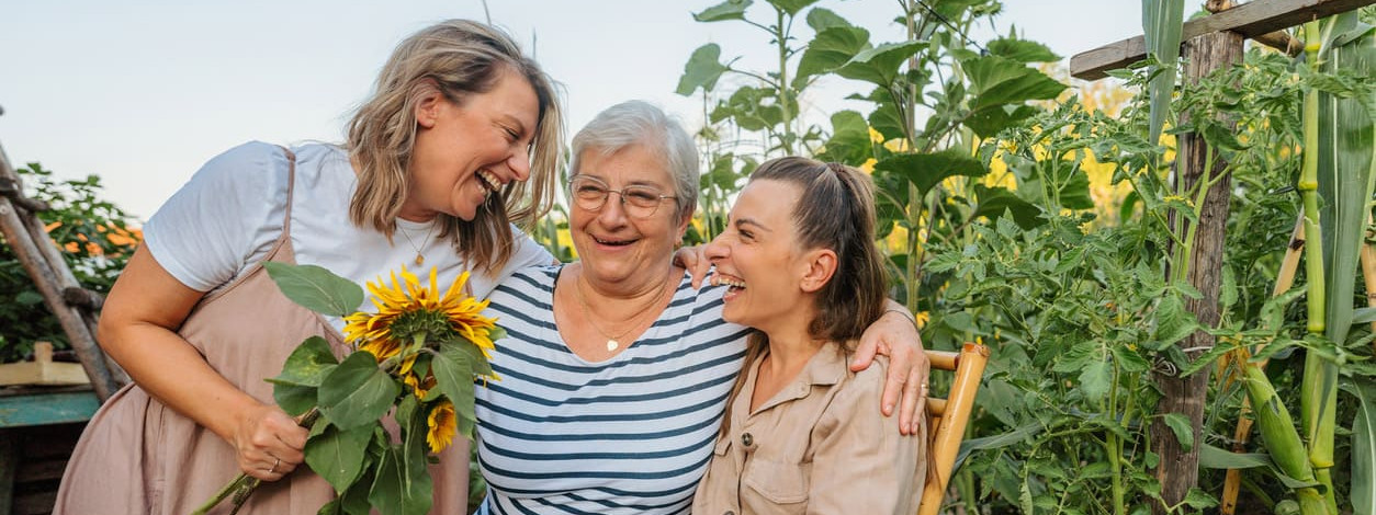 Eine Seniorin und ihre Töchter sitzen im Garten und lachen gemeinsam