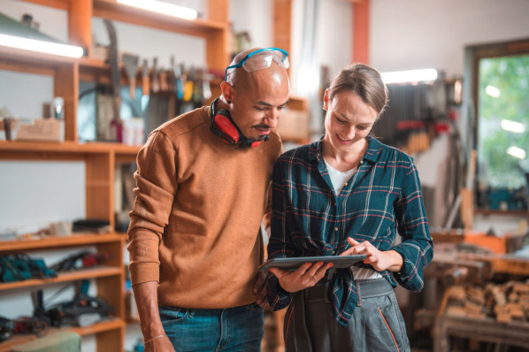 Zwei Beschäftigte stehen in einer Werkstatt und schauen gemeinsam auf ein Tablet.