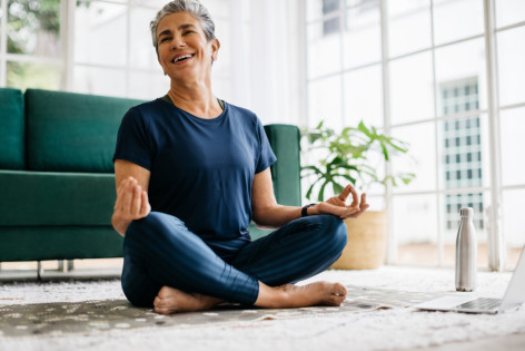  Seniorin lächelt, während sie zu Hause Yoga praktiziert