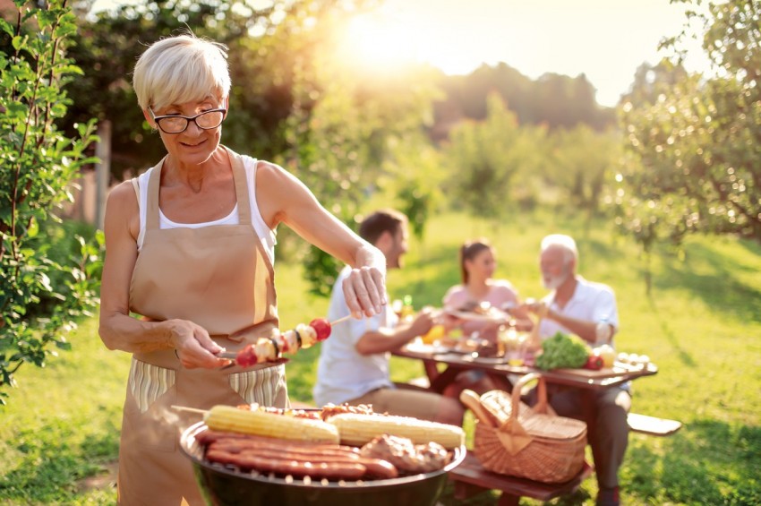 Familie grillt im Sommer im Garten. Oma wendet die gesunden Gemüsespieße.