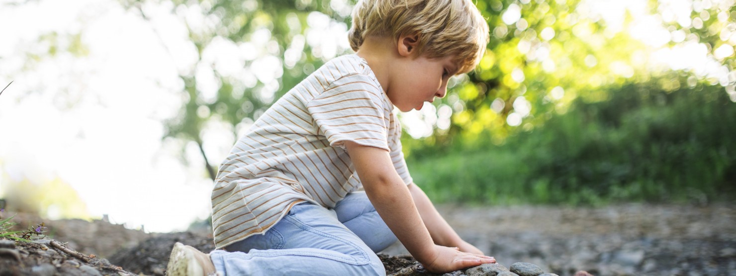 Ein 4 jähriger Junge spielt draußen auf dem Boden mit Steinen