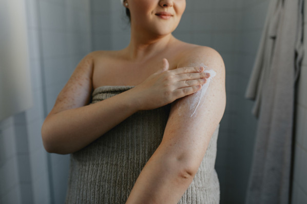 Frau cremt nach dem Duschen ihren Oberarm mit Feuchtigkeits-Lotion ein