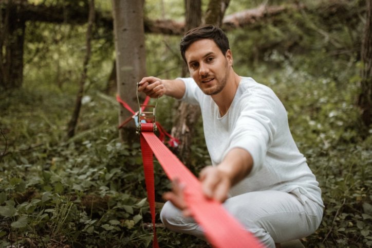 Ein Mann spannt eine Slackline am Baum.