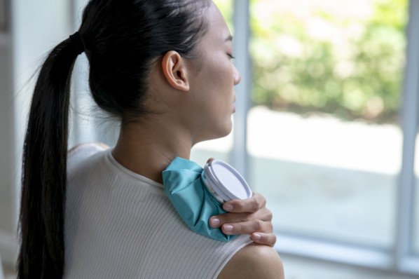 Asian woman putting a hot water bottle on her shoulder pain.