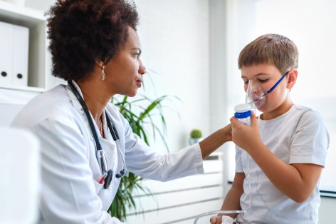 Eine etwas 40 jährige Ärztin behandelt einen 10 jährigen Jungen. der Junge inhaliert mit einem Inhalationsgerät.