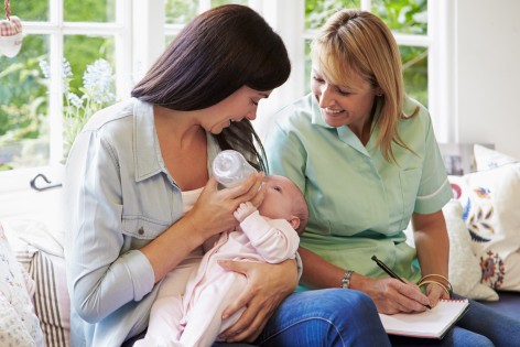 Zwei Frauen füttern ein Baby mit Flasche.