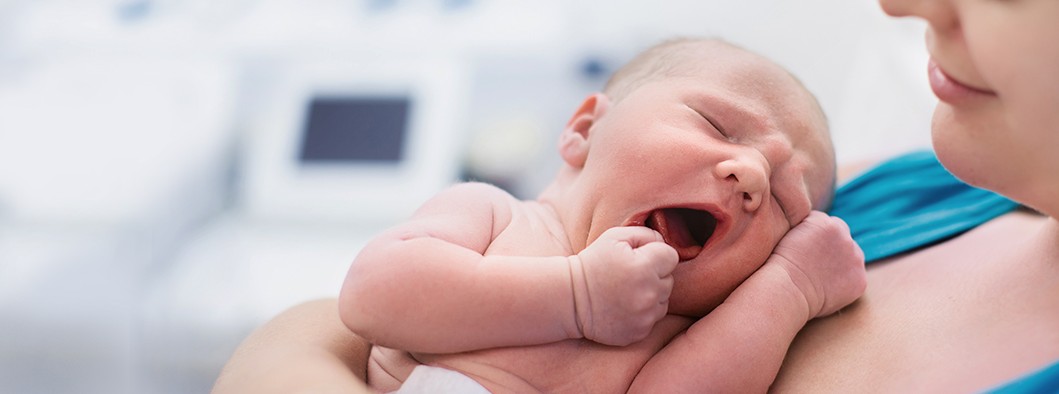 Mutter hält lächelnd ihr neu geborenes Baby im Arm.