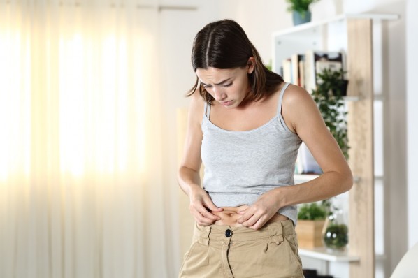 Ein junges Mädchen drückt mit den händen eine Speckfalte am Bauch zusammen