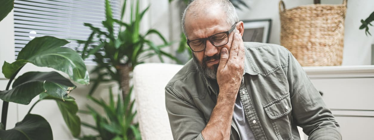 Ein älterer Mann verspürt aufgrund von Zähneknirschen Schmerzen im Kiefer
