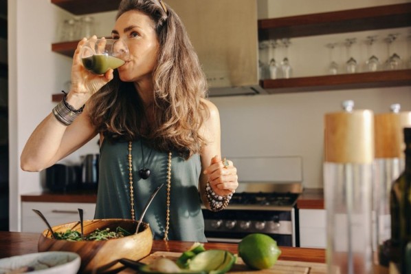 Vegane Frau trinkt grünen Saft in ihrer Küche.