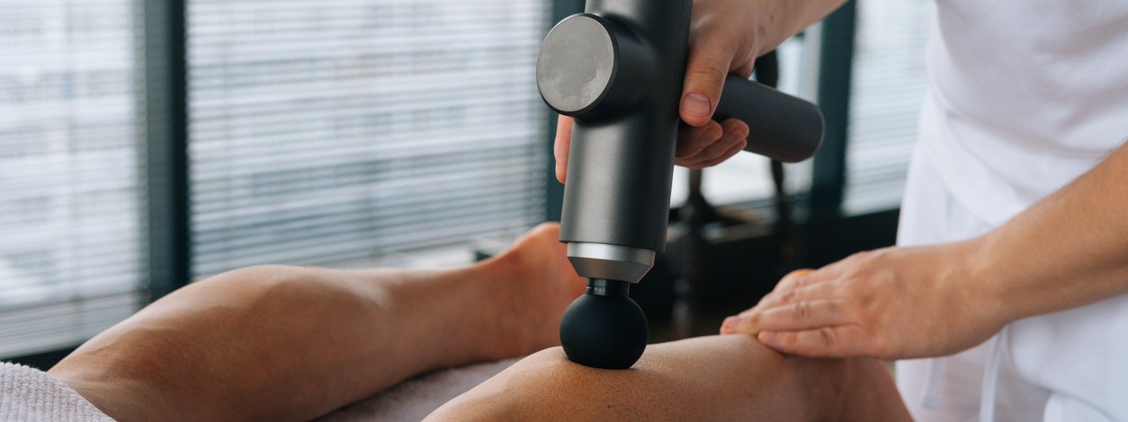 Eine Massagepistole wird am Bein angewendet