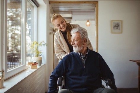 Eine Angehörige schiebt einen älteren pflegebedürftigen Mann im Rollstuhl.