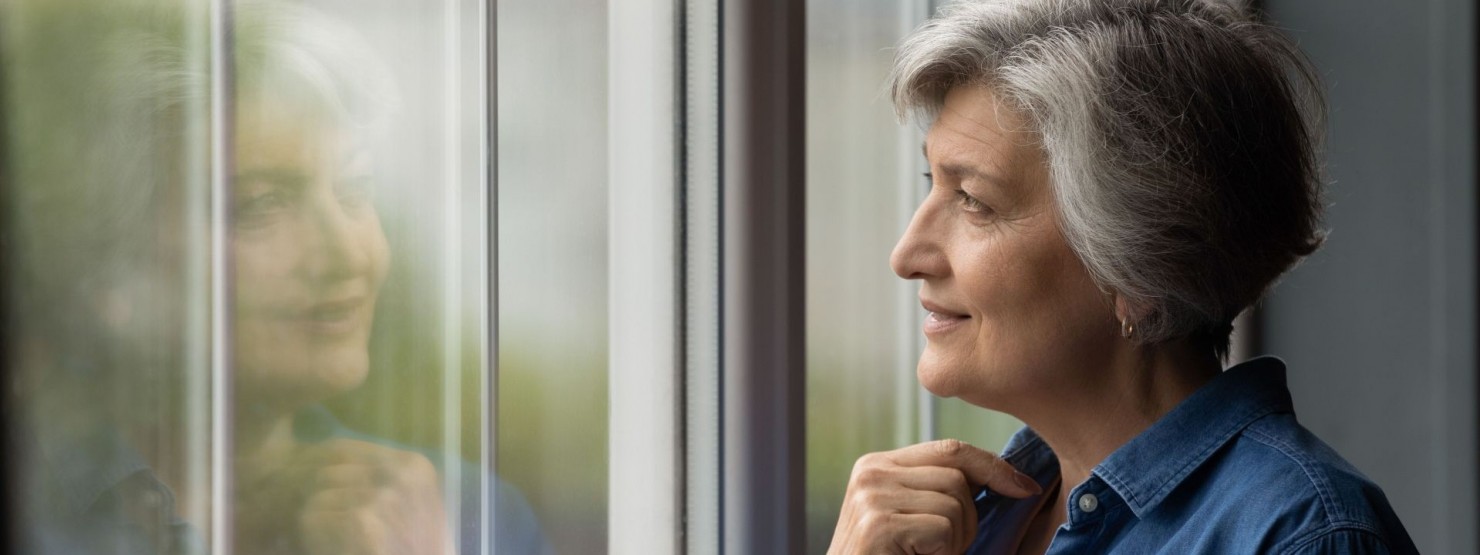 Älterre Frau Anfang 60 schaut mit einem leichten Lächeln aus dem fenster