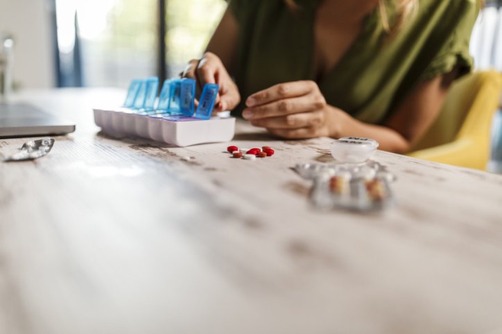 Close up shot of unrecognizable woman arranging her prescription medication in a weekly pill organizer.