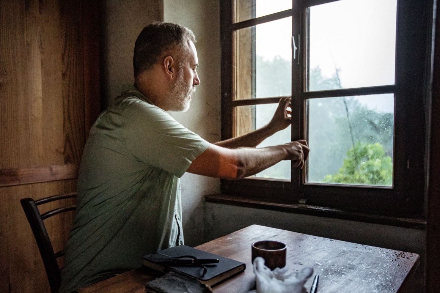Ein Mann sitzt an einem Tisch und öffnet ein Fenster zum Lüften.