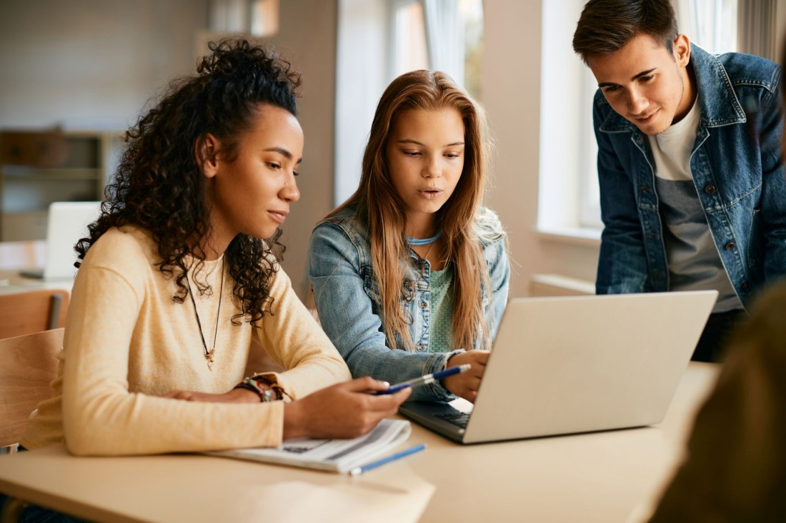 Drei Teenager lesen im Klassenchat über einen Laptop.