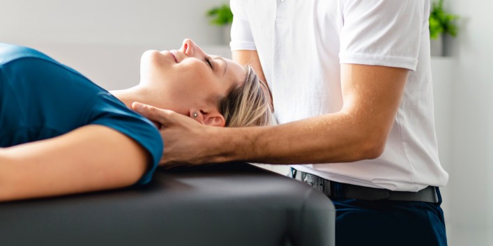 Therapeut behandelt den Nacken einer circa 30-jährigen Patientin.