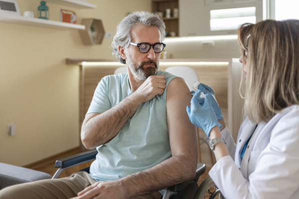 Disabled Male Patient Sitting in the Wheelchair Getting Vaccinated at His Home by Female Doctor