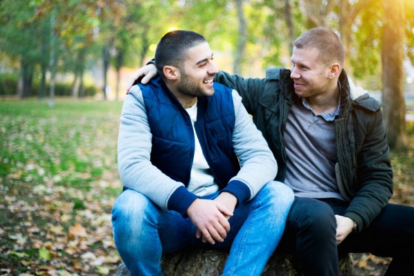 Zwei etwa 35-jährige Freunde sitzen im Park auf einer Bank und unterhalten sich.