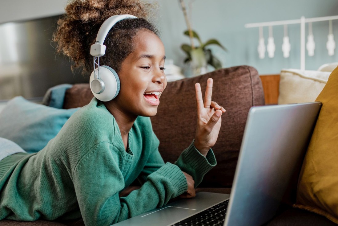 Ein etwa 8-jähriges Mädchen zeigt zwei Finger in eine Laptopkamera.