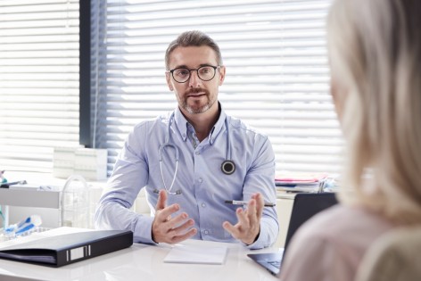 Ein Arzt sitzt an einem Schreibtisch und berät einen Patienten.