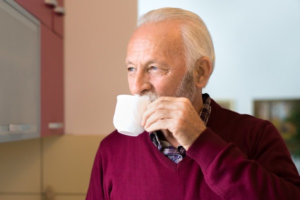 ca 70-jähriger Mann im roten Pullover trinkt aus einer weißen tasse