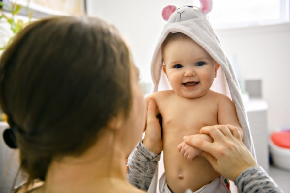 Mutter und Baby, das ein Kapuzenhandtuch trägt und lacht.