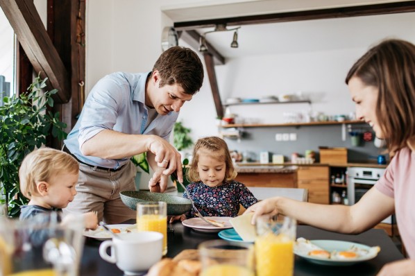 Vater serviert Spiegelei zum Frühstück mit Frau und zwei kleinen Kindern