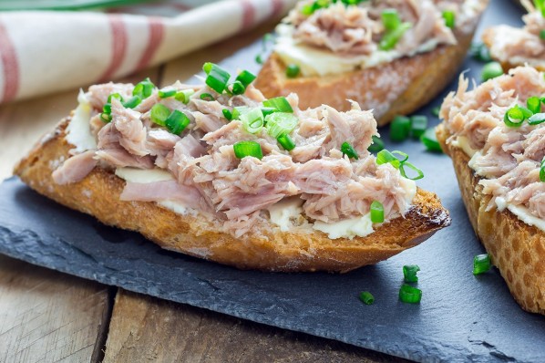 Baguettescheiben mit Thunfischsalat und Schnittlauch auf einem Tisch.