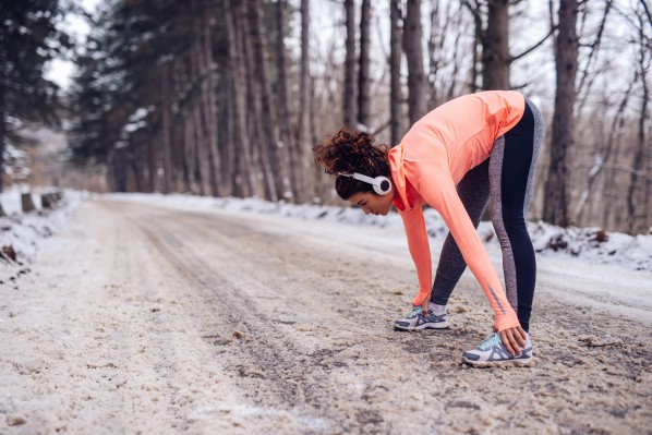Junge Frau Anfang 20 wärmt sich vor dem joggen im Winterwald auf