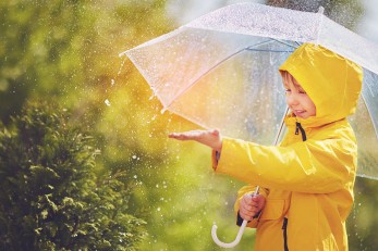 Ein Junge mit Regenschirm und gelben Regenmantel genießt den Regen