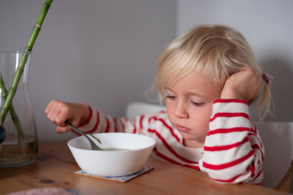 Ein kleines Mädchen sitzt vor ihrer Suppenschüssel und möchte nicht essen.