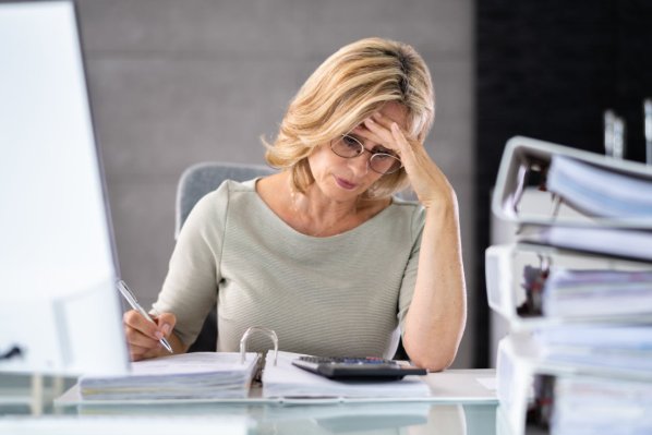 Eine Beschäftigte sitzt am Arbeitsplatz und stützt gestresst ihren Kopf in die Hand.