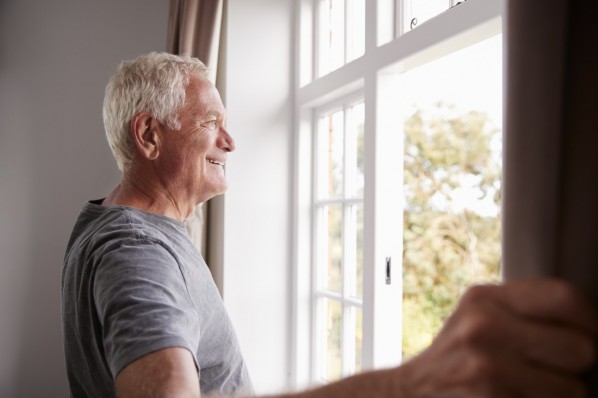 Senior Man Opening Bedroom Curtains And Looking Out Of Window