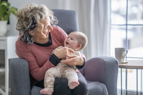 Eine Seniorin hält ein frisch gegen RS-Virus geimpftes Baby auf dem Schoß.