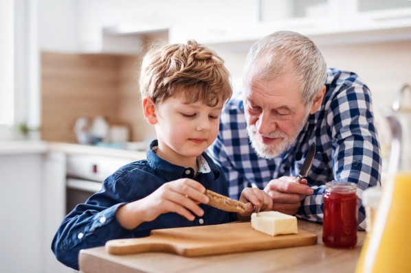 Großvater sieht seinem etwa 5-jährigen Enkel dabei zu, wie er Butter auf ein Brot schmiert.