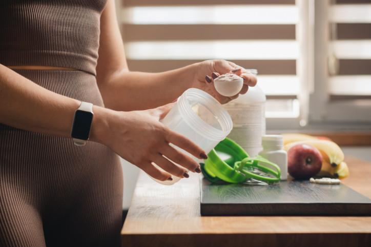 Eine Sportlerin dosiert Kreatin in einen Shaker.