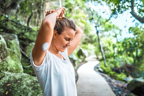 Sportliche Frau Mitte 20 mit einem Sensor am Unterarm bereitet sich auf ihren Waldlauf vor und bindet sich die Haare zusammen.