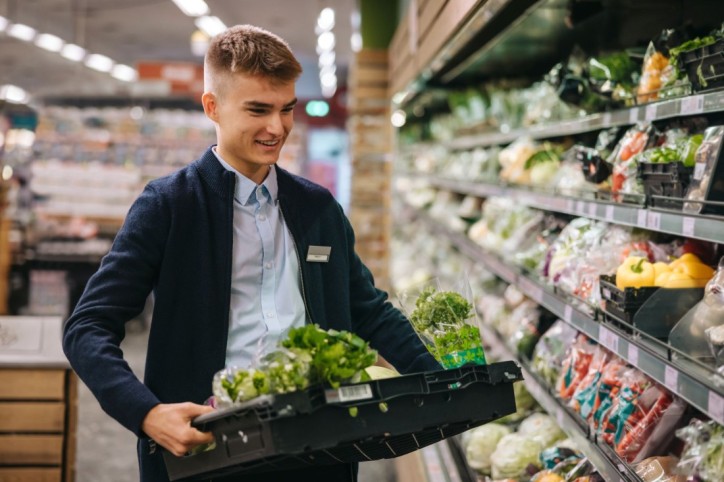 Ein Lehrling räumt frische Kräuter im Supermarktregal ein.