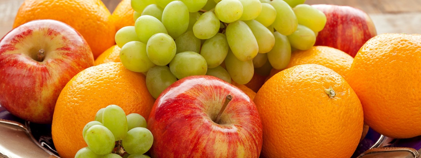 Eine Obstschale mit Weintrauben, Äpfeln und Orangen steht auf einem Tisch.