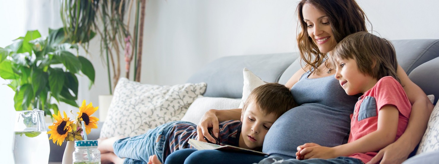 Schwangere Frau sitzt mit zwei Kindern auf dem Sofa