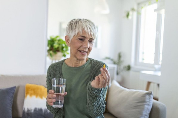 Frau mit Wasserglas in der Hand, die eine Tablette nimmt.