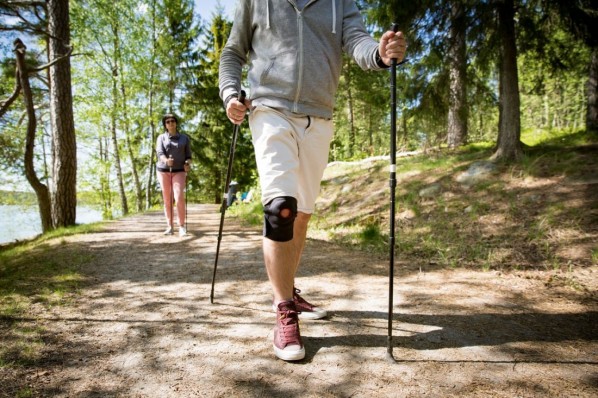 Mann läuft im Wald mit Nordic-Walking Stöcken. Er trägt dabei eine Kniebandage. 