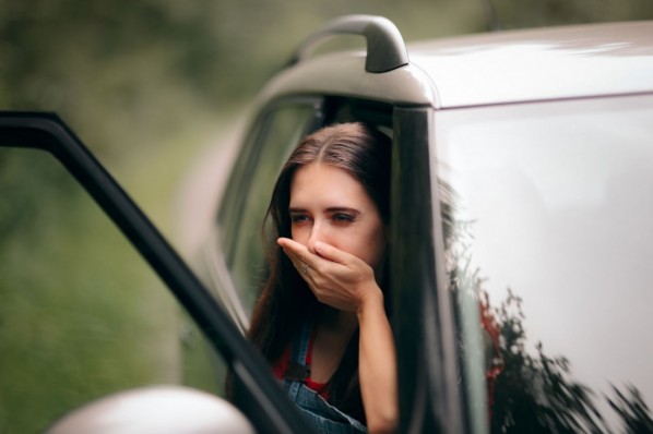 Junge Frau sitzt im parkenden Auto und leidet an Übelkeit. 
