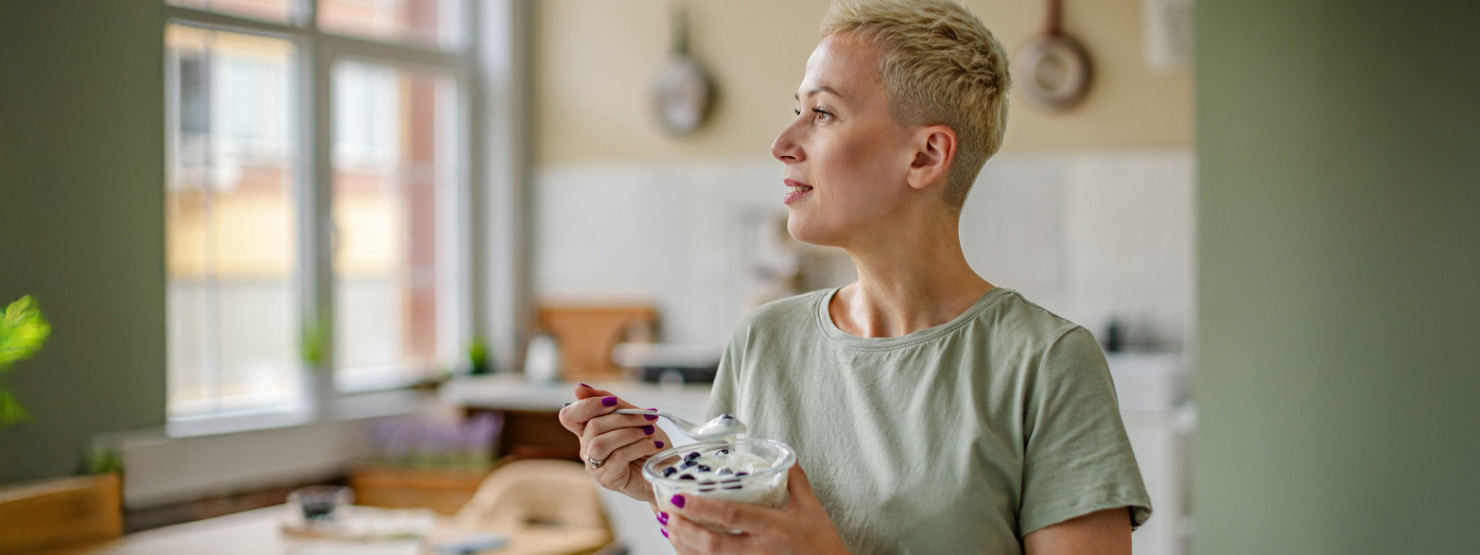 Frau genießt morgens eine Schüssel mit Quark und frischen Blaubeeren in einer gemütlichen Küche