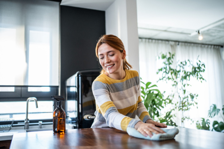 Lächelnde Frau, die Holztisch in moderner Küche reinigt