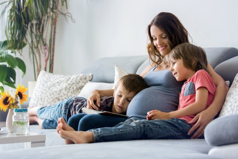 Schwangere Frau sitzt mit zwei Kindern auf dem Sofa