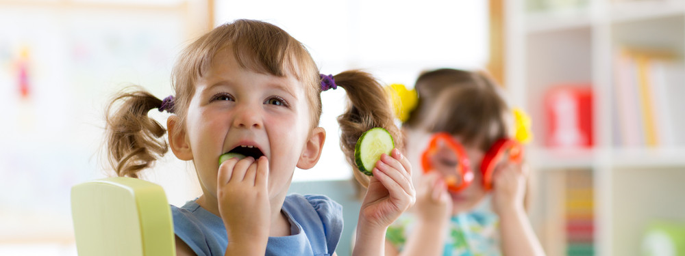 Ein Kindergartenkind steckt sich Gurkenscheiben in den Mund.