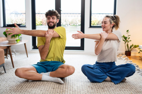 A happy couple engaged in stretching exercises during a relaxing yoga session at home.